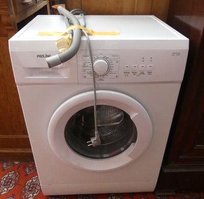 une machine à laver blanche à laquelle est raccordé un tuyau
