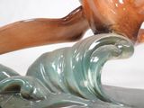 a ceramic sculpture of a bird that is flying over a wave