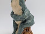 a ceramic frog sitting on top of a piece of wood