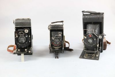 three old cameras sitting side by side on a white surface