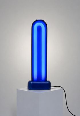 une lampe bleue posée sur un socle blanc, près d'un mur
