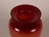 a red vase sitting on a table with a white wall in the background