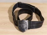 une ceinture noire munie d'une boucle métallique posée sur une table en bois