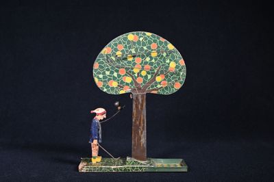 une petite figurine représentant un homme debout près d'un arbre chargé d'oranges