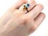 la main d'une femme tenant une bague sertie d'une pierre bleue et jaune