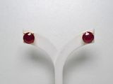une paire de boucles d'oreilles à clous ornées de pierres rouges, posée sur un présentoir blanc