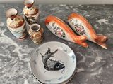 une assiette décorée d'un motif de poisson, à côté de quelques vases et d'une autre assiette décorée d'un motif de poisson