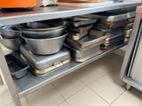 Plusieurs casseroles et poêles sont empilées sur une étagère métallique dans une cuisine.