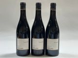 trois bouteilles de vin rouge sont posées sur une surface blanche