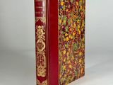 an old book with a red cover sitting on top of a white table