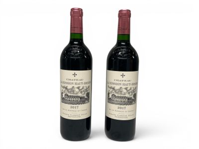 two bottles of red wine sitting next to each other on a white surface