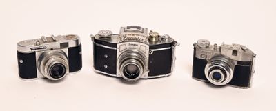 three old cameras sitting side by side on a white surface