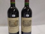two bottles of red wine sitting on top of a white table