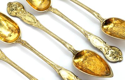 six gold spoons with ornate designs are lined up on a white surface