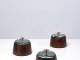 trois petits bols en bois avec des couvercles en verre, posés sur une surface blanche