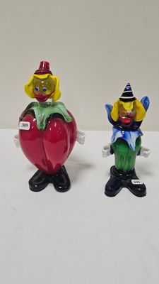 two figurines of clowns sitting on top of a red apple
