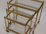 three brass and glass nesting tables on casteors on a white background