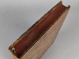 an old book with a red cover sitting on top of a white surface