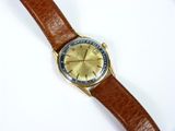 gros plan d'une montre sur une surface blanche avec un bracelet marron