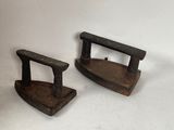 two old iron ironing tools sitting on a white surface