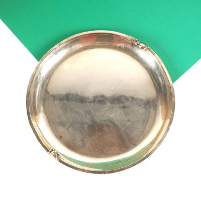 une petite assiette en argent posée sur un fond vert