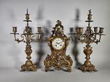 trois bougeoirs dorés et une horloge posés sur une table