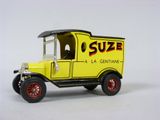 un petit camion jouet jaune avec des roues rouges et des jantes rouges, posé sur une surface blanche