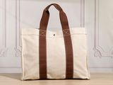 a white canvas tote bag with brown leather handles on a wooden floor