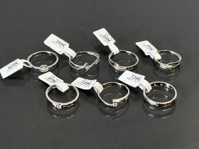 six bagues en argent munies d'étiquettes, posées sur une surface noire