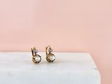 une paire de boucles d'oreilles en or ornées de pierres blanches, posées sur un bloc de marbre