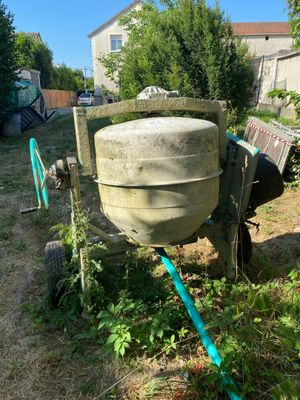 une bétonnière dans la cour, à laquelle est raccordé un tuyau d'arrosage
