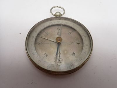 une vieille boussole en argent posée sur une surface blanche, sur fond blanc