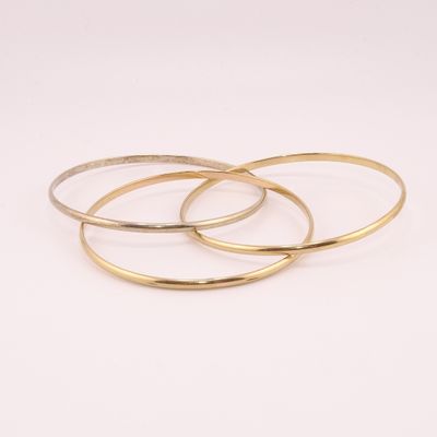 un ensemble de trois bracelets rigides dorés sur fond blanc