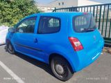 the small blue car is parked in the parking lot near a fence