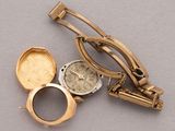 a gold watch and a gold tie bar on a gray surface
