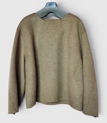 Le pull est suspendu à un cintre accroché à un mur blanc.