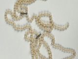 un collier de perles blanches muni d'un fermoir en argent, posé sur un fond blanc