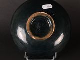 a black vase with a gold rim sitting on a stand