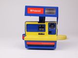 un appareil photo Polaroid jaune et bleu posé sur une surface blanche