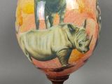 une image représentant un rhinocéros posé sur un globe terrestre, lui-même posé sur un socle en bois