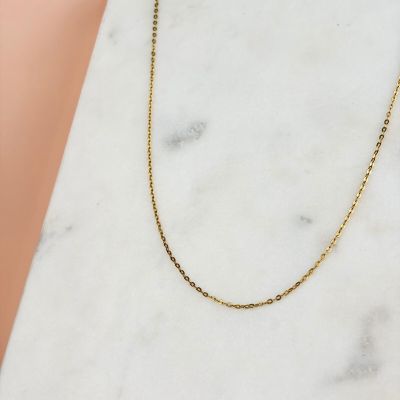 un collier à chaîne en or posé sur une surface en marbre