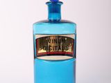 une bouteille en verre bleue ornée d'une étiquette dorée, posée sur une surface blanche