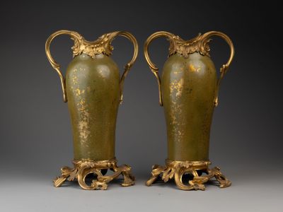 Deux vases verts munis d'anses sont posés sur une surface grise.