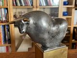 une statue en bronze représentant un taureau, posée sur une table en bois