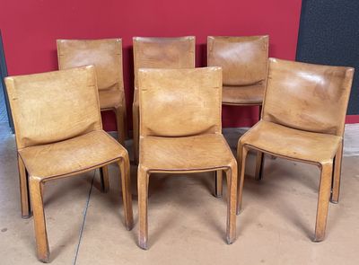 Quatre fauteuils en cuir sont alignés contre un mur rouge