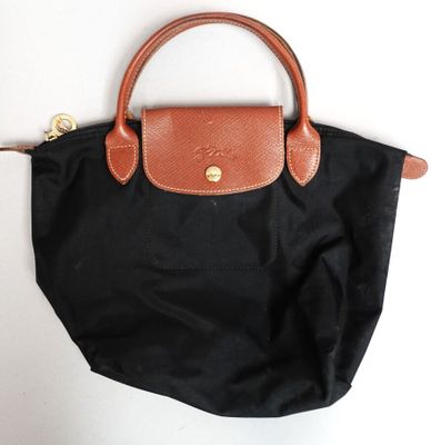 un sac à main noir muni d'une poignée marron, posé sur une surface blanche