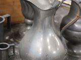 a silver pitcher sitting on a table next to other silver vases