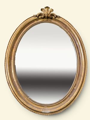 un miroir ovale avec un cadre doré accroché à un mur blanc