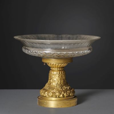 an antique glass bowl on a gold pedestal with a black background
