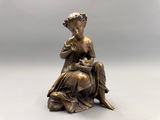 une statue en bronze représentant une femme assise sur un rocher, une fleur à la main